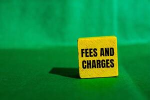 Fees and charges message written on yellow wooden cube with green background. Conceptual fees and charges symbol. Copy space. photo