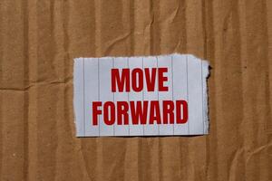 Move forward message written on ripped torn paper piece with cardboard paper background. Conceptual move forward symbol. Copy space. photo