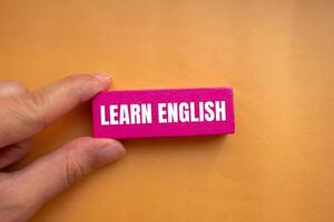 Learn english message written on pink wooden block with orange background. Conceptual learn english symbol. Copy space. photo