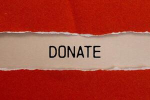 Donate message written on ripped torn red paper with beige background. Conceptual donate symbol. Copy space. photo