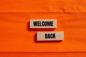 Welcome back message written on wooden blocks with orange background. Conceptual welcome back symbol. Copy space. photo