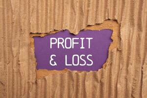 Profit and loss message written on ripped torn cardboard paper with purple background. Conceptual profit and loss symbol. Copy space. photo