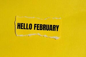 Hello february message written on ripped yellow torn paper piece with yellow background. Conceptual hello february symbol. Copy space. photo