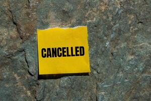Cancelled message written on ripped torn yellow paper piece with stone background. Conceptual cancelled symbol. Copy space. photo