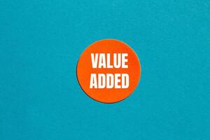 Value added message written on round orange sticker with blue background. Conceptual value added symbol. Copy space. photo