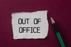 Out of office message written on ripped torn paper piece with purple background. Conceptual out of office symbol. Copy space. photo