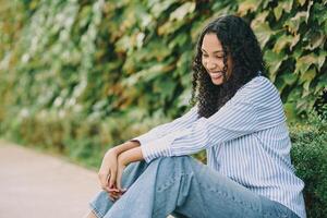 A Smiling Young Woman Sitting Outdoors, Surrounded by Lush Greenery in a Beautiful Setting photo