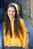 A cheerful woman in a yellow sweater posed in an urban setting with vibrant city colors photo