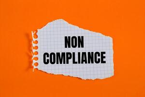 Non compliance message written on ripped torn checkered graph paper piece with orange background. Conceptual non compliance symbol. Copy space. photo