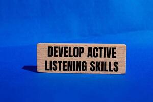 Develop active listening skills message written on wooden block with blue background. Conceptual develop active listening skills symbol. Copy space. photo