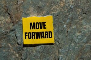 Move forward message written on ripped torn yellow paper piece with stone background. Conceptual move forward symbol. Copy space. photo
