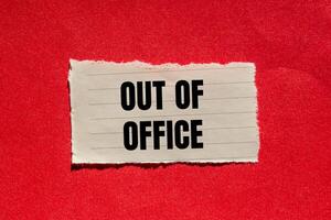 Out of office message written on ripped torn paper piece with red background. Conceptual out of office symbol. Copy space. photo