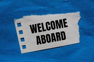 Welcome aboard message written on ripped torn paper piece with blue background. Conceptual welcome aboard symbol. Copy space. photo