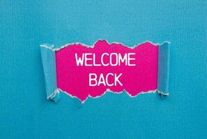 Welcome back message written on ripped torn blue paper with pink background. Conceptual welcome back symbol. Copy space. photo