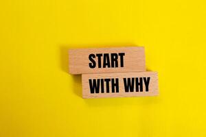 Start with why message written on wooden blocks with yellow background. Conceptual start with why symbol. Copy space. photo