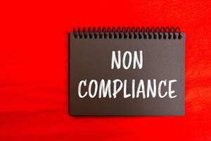 Non compliance message written on black notebook page with red background. Conceptual non compliance symbol. Copy space. photo
