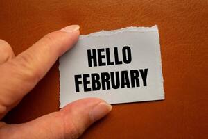 Hello february message written on ripped torn paper piece with brown background. Conceptual hello february symbol. Copy space. photo