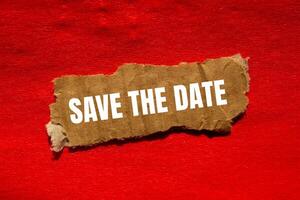 Save the date message written on ripped torn cardbaord paper piece with red background. Conceptual save the date symbol. Copy space. photo