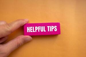 Helpful tips message written on pink wooden block with orange background. Conceptual helpful tips symbol. Copy space. photo