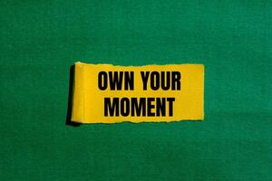Own your moment message written on ripped torn yellow paper piece with green background. Conceptual own your moment symbol. Copy space. photo