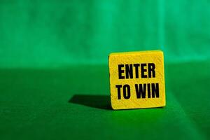 Enter to win message written on yellow wooden cube with green background. Conceptual enter to win symbol. Copy space. photo