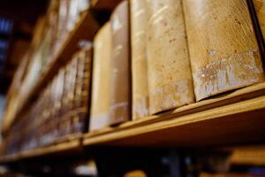 Row of aged leather-bound books on wooden shelf in library photo