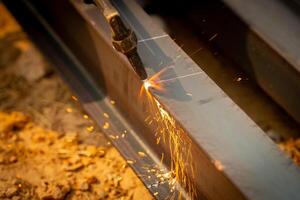 Skilled welder cuts metal with a gas torch in industrial workshop. Sparks fly during precision fabrication process. Craftsman control and expertise in metalworking. Gas torch cuts through steel. photo