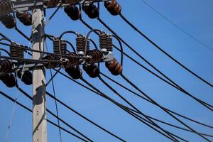 Modern electrical power infrastructure detail showing high voltage transmission lines and ceramic insulators against clear blue sky demonstrating energy distribution. Industrial power grid equipment. photo