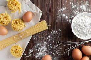 Raw pasta tagliatelle, spaghetti with eggs and flour on wooden background. photo