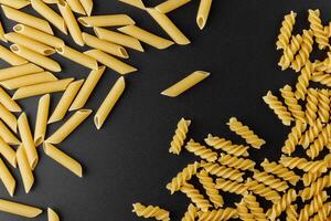 Raw pasta penne rigate and fusilli with copy space on black background. photo
