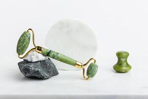 Green jade roller massager for face on white marble. photo