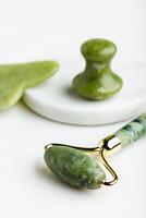 Green jade roller massagers for face on white marble. photo