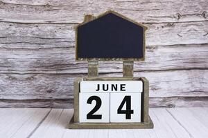Chalkboard with June 24 date on white cube block on wooden table. photo