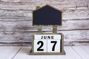 Chalkboard with June 27 date on white cube block on wooden table. photo