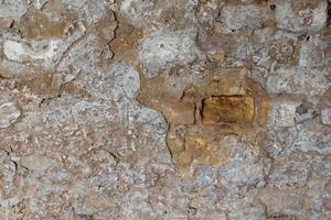 Weathered stone wall showing cracked texture and exposed bricks in an old building photo
