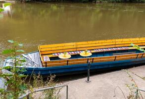 Boat with yellow bench seating docked by the river at a peaceful location surrounded by greenery during daytime photo