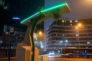 An electric bus stands at an empty bus stop and charges, a close up photo
