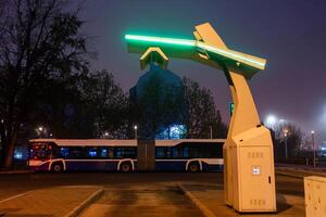 An electric bus stands at an empty bus stop and charges, a close up photo