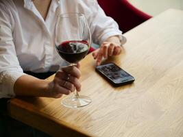 A woman holding a glass of wine and a cell phone photo