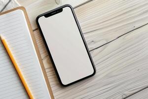 A smartphone sits on a wooden tabletop with a blank screen, accompanied by a notepad and a pencil, inviting ideas and creativity in a serene workspace photo
