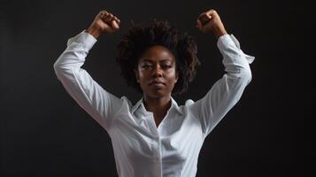 A confident woman stands with her arms raised, expressing strength and determination. The dark background emphasizes her powerful presence during a moment of empowerment photo