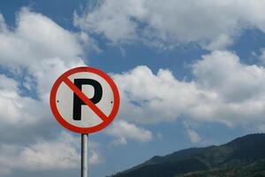 No Parking sign post with cloudy sky and hill background. A round signpost on the side of the road. Copy Space. Graphic Resources. Road Traffic Signs. Red Signs photo