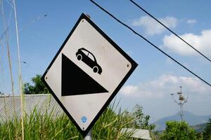 Warning Dangerous road descent sign post with cloudy sky and electric cables background. Rhombus signpost on the side of the road. Copy Space. Graphic Resources. Road Traffic Signs. Black Signs photo