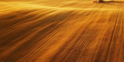 Aerial View of Golden Agricultural Field with Farming Equipment Working Through Streaks of Soil and Light During Sunset in Rural Landscape photo