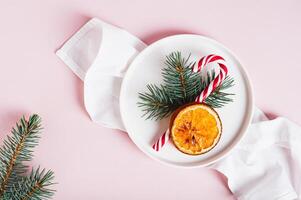 Close up of christmas table setting lollipop, fir tree and dried orange on plate on table top view photo