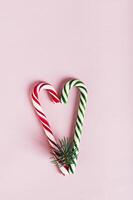 Heart made of red and green candy canes and fir branches on pink top and vertical view photo