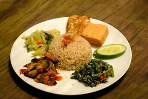 Nasi Campur Vegetarian is is brown rice with sauted green vegetables, sambal, fresh cucumber and tomato slices, fried tofu, and fried tempeh. Suitable for vegetarians. Indonesian food. Nasi Rames. photo