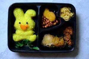 Nasi Kuning is Indonesian tradiotional yellow rice, made of turmeric, coconut milk, spices. Served with beef floss, crackers, sliced omelet, fried peanuts, fried tempeh. Street food. Bento. photo