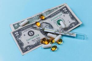Medical thermometer on the background of pills and paper money. Blue background photo