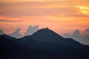 a mountain with a tree on it and a pink sky in the background. photo